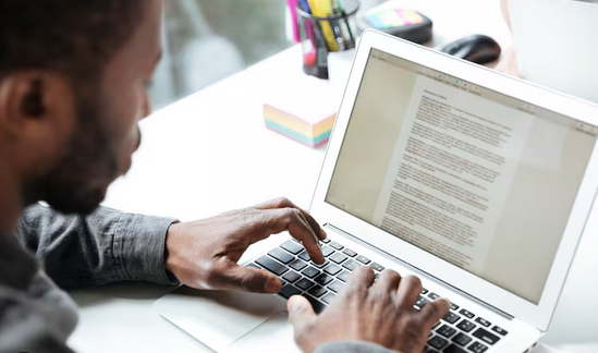 A man is focused on typing on a laptop computer, with his hands positioned over the keyboard. 